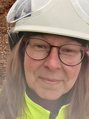 En kvinna med skyddshj&auml;lm ser in i kameran, hon ser glad ut