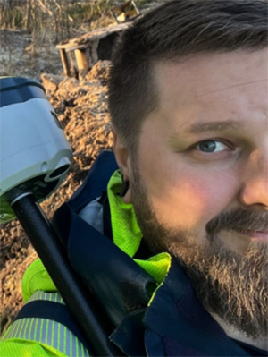 En man med sk&auml;gg ler in i kameran